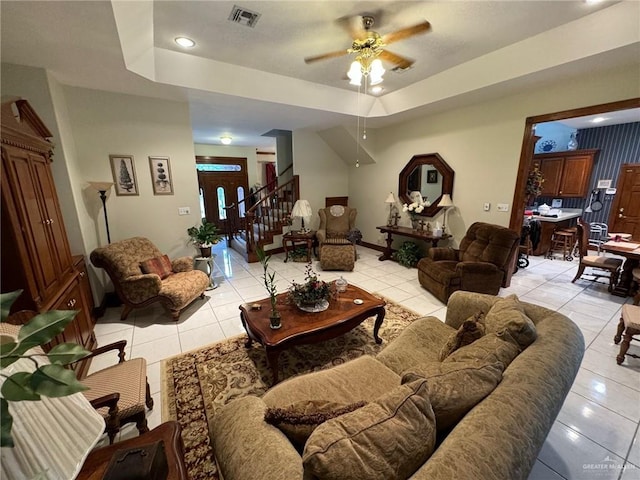 tiled living room with ceiling fan and a tray ceiling