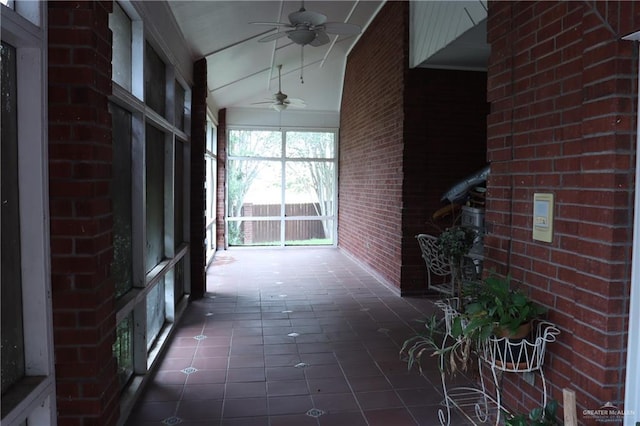 hall featuring brick wall, vaulted ceiling, and dark tile patterned floors