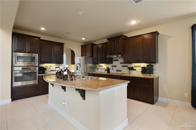 3502 Plantation Grove Blvd, Mission, TX 78572 - kitchen with stainless steel appliances, arched walkways, under cabinet range hood, a center island with sink, and a breakfast bar area