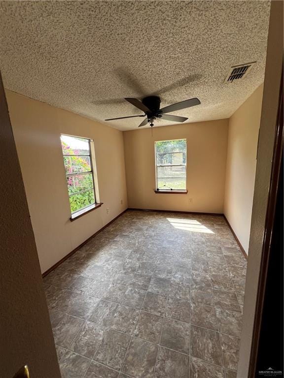 unfurnished room featuring a wealth of natural light, ceiling fan, and a textured ceiling