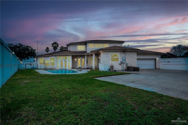 5501 N 8th St, Mcallen, TX 78504 - back of house at dusk with central AC unit, a fenced backyard, concrete driveway, an attached garage, and a lawn