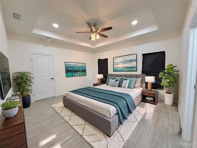 bedroom featuring a raised ceiling, ceiling fan, and light wood-type flooring