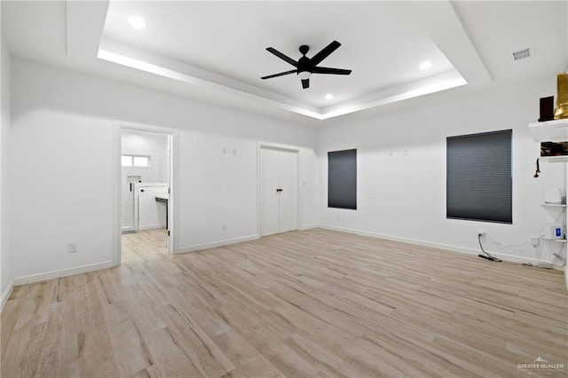 unfurnished living room featuring a tray ceiling, light hardwood / wood-style flooring, and ceiling fan