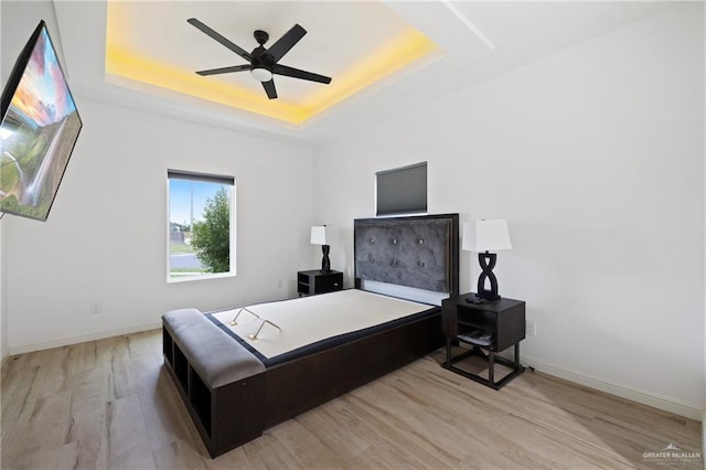 bedroom with light wood-type flooring, a tray ceiling, and ceiling fan