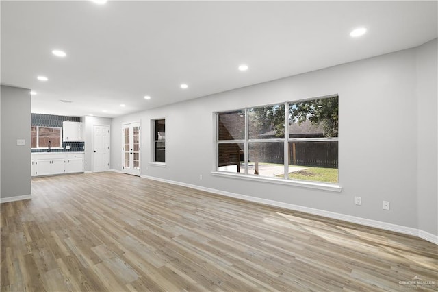 unfurnished living room with light wood-type flooring, sink, and a wealth of natural light