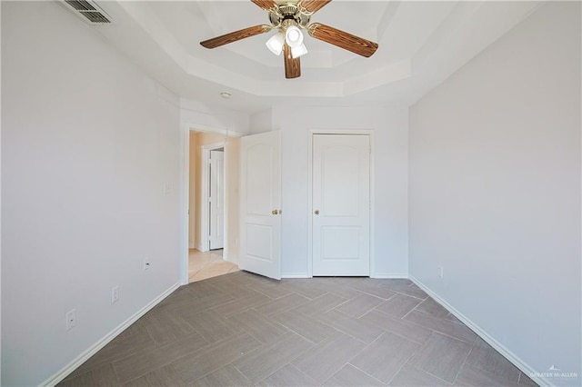 unfurnished bedroom with ceiling fan and a tray ceiling