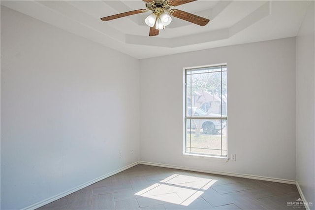 empty room featuring parquet floors, ceiling fan, and a tray ceiling