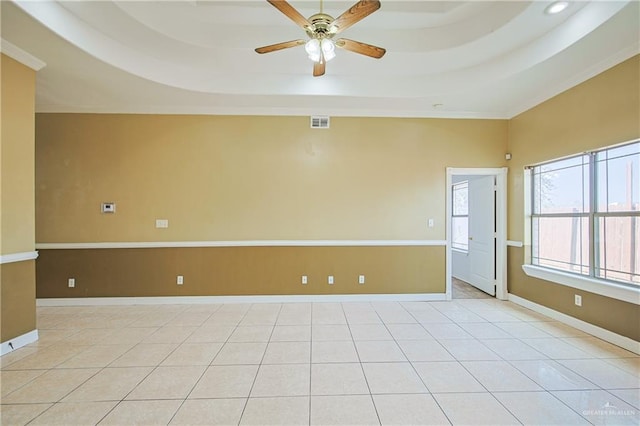 tiled empty room with crown molding, a tray ceiling, and ceiling fan