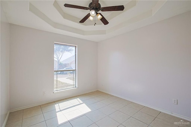 empty room featuring ceiling fan, a tray ceiling, and light tile patterned floors