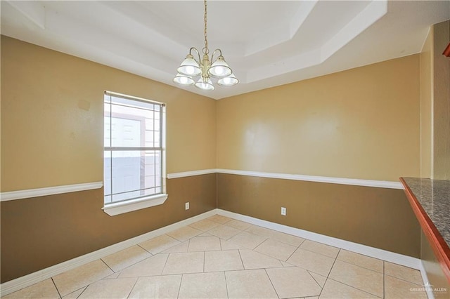 tiled empty room featuring a tray ceiling and a chandelier