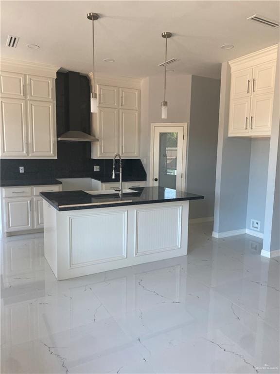 kitchen with white cabinetry, a center island with sink, decorative light fixtures, and wall chimney range hood