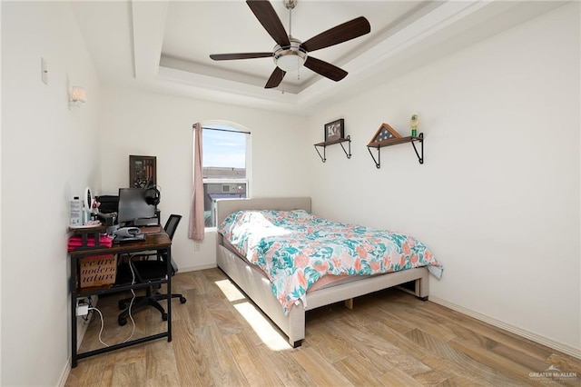 bedroom featuring light wood-type flooring, a raised ceiling, and ceiling fan