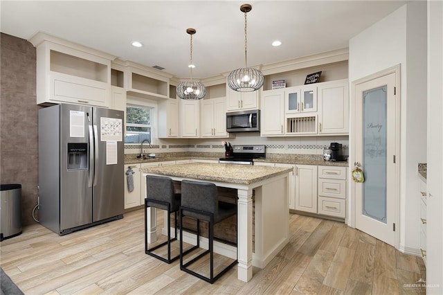 kitchen with light stone counters, pendant lighting, a center island, stainless steel appliances, and white cabinetry