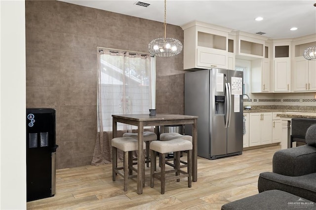 kitchen featuring white cabinets, hanging light fixtures, light wood-type flooring, and stainless steel refrigerator with ice dispenser