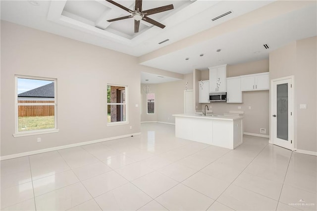 kitchen featuring ceiling fan, light tile patterned floors, a tray ceiling, a kitchen island with sink, and white cabinets