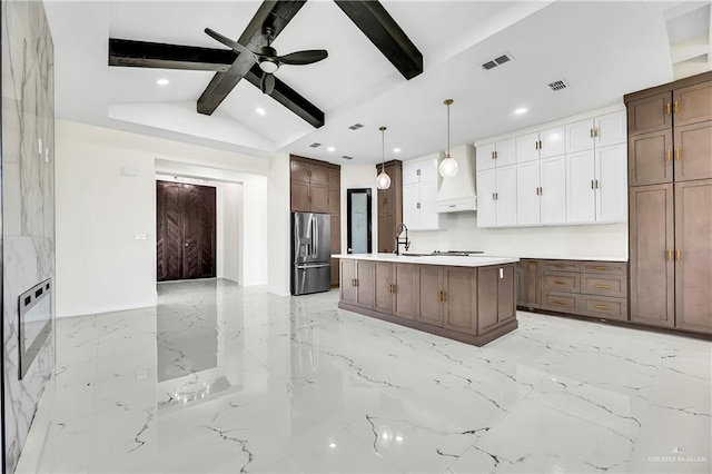 kitchen featuring white cabinetry, vaulted ceiling with beams, stainless steel fridge, an island with sink, and decorative light fixtures