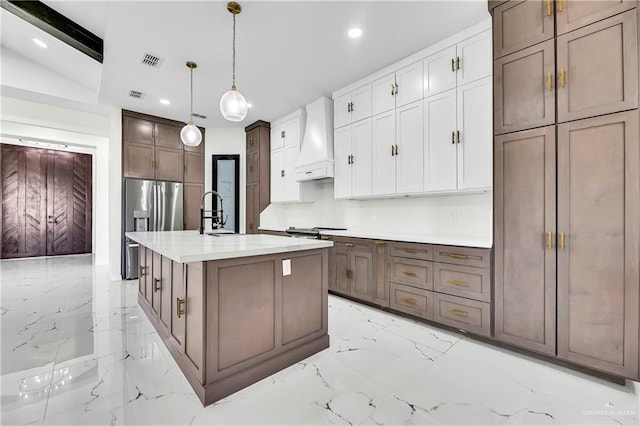 kitchen with hanging light fixtures, lofted ceiling, a center island with sink, white cabinets, and custom range hood