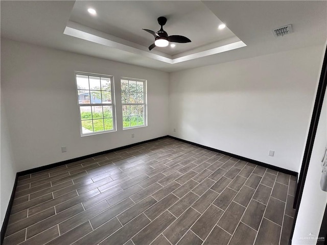 empty room featuring a ceiling fan, a raised ceiling, baseboards, and visible vents