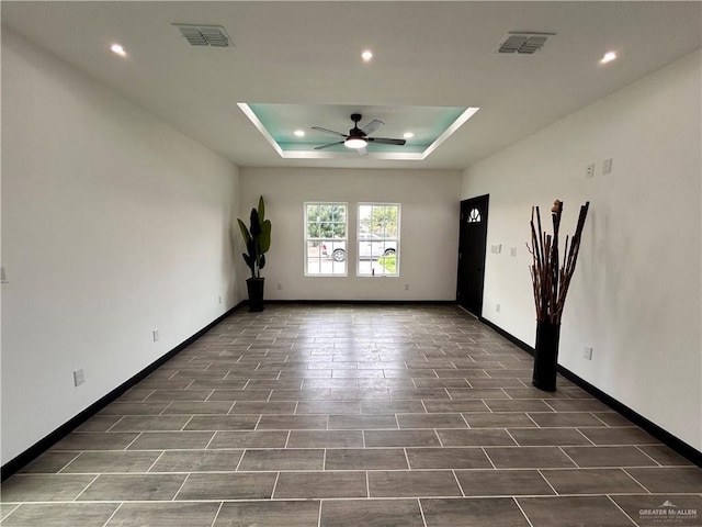 spare room featuring a raised ceiling, a ceiling fan, visible vents, and baseboards