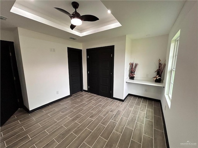 unfurnished bedroom featuring a ceiling fan, visible vents, baseboards, wood finish floors, and a raised ceiling