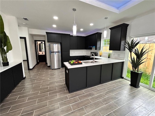 kitchen featuring a peninsula, freestanding refrigerator, a sink, light countertops, and dark cabinets