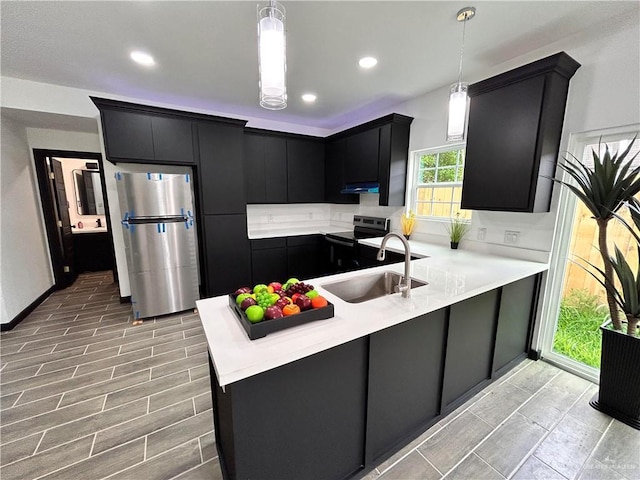 kitchen featuring a sink, dark cabinetry, a peninsula, appliances with stainless steel finishes, and light countertops