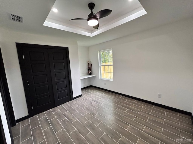 empty room with visible vents, ceiling fan, baseboards, wood tiled floor, and a raised ceiling