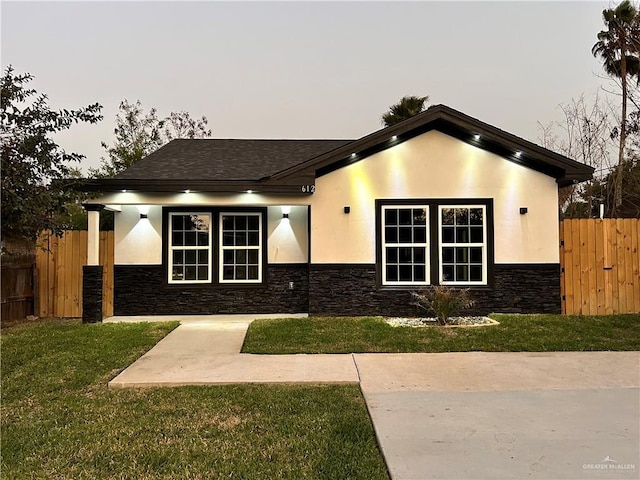 view of front of house with stone siding, stucco siding, a front yard, and fence