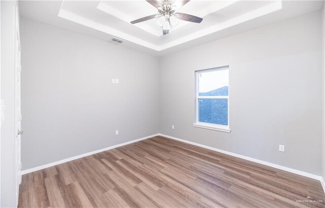 empty room featuring a tray ceiling, ceiling fan, and light hardwood / wood-style floors