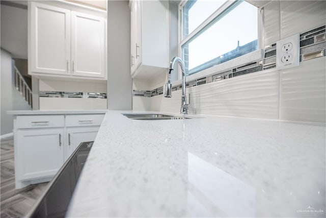 kitchen featuring backsplash, white cabinetry, sink, and light stone countertops