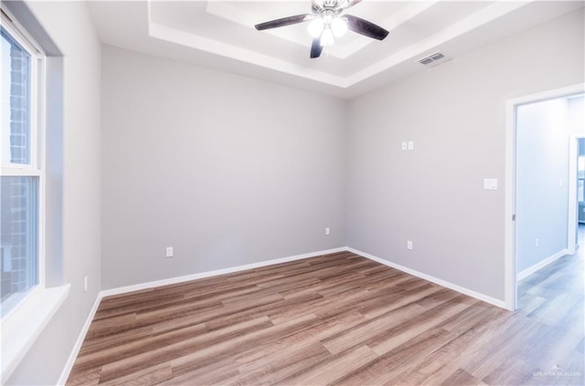 empty room featuring ceiling fan, a raised ceiling, and light wood-type flooring