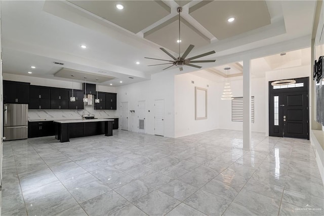 interior space with pendant lighting, stainless steel refrigerator, an island with sink, a kitchen breakfast bar, and coffered ceiling