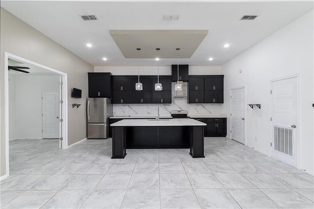 kitchen featuring an island with sink, sink, decorative backsplash, hanging light fixtures, and stainless steel appliances