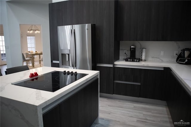 kitchen featuring a kitchen island, tasteful backsplash, stainless steel fridge, black electric stovetop, and light wood-type flooring