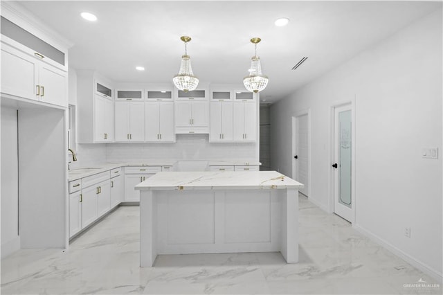 kitchen featuring pendant lighting, light stone countertops, white cabinets, a kitchen island, and decorative backsplash