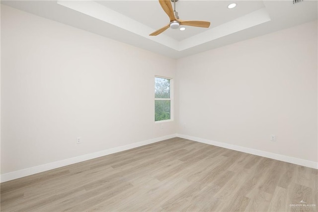 empty room featuring a tray ceiling, ceiling fan, and light wood-type flooring