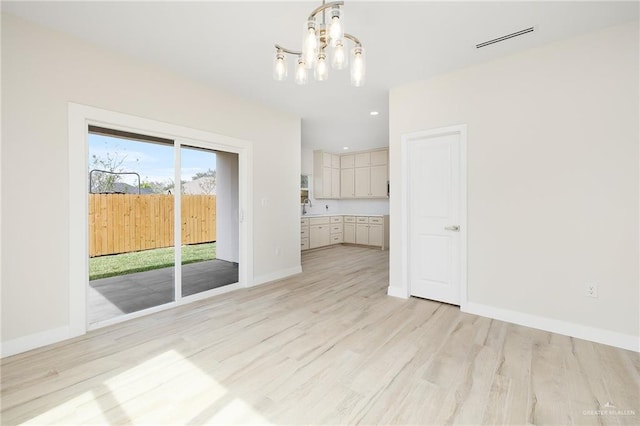 unfurnished living room featuring sink, a notable chandelier, and light hardwood / wood-style flooring