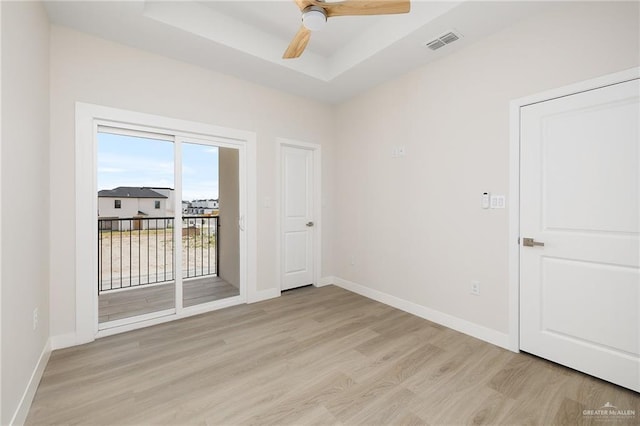 empty room with ceiling fan, a tray ceiling, and light wood-type flooring