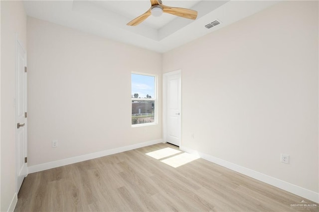 empty room featuring a raised ceiling, ceiling fan, and light hardwood / wood-style floors