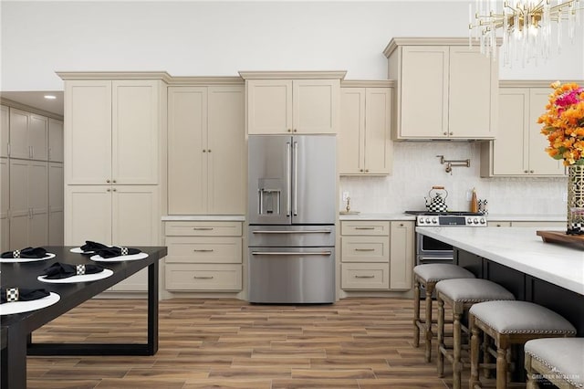 kitchen with hanging light fixtures, stainless steel appliances, cream cabinets, and tasteful backsplash