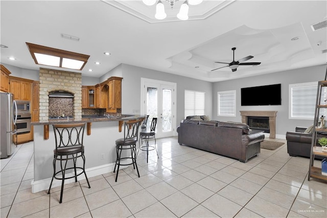 kitchen featuring light tile patterned floors, a raised ceiling, a glass covered fireplace, appliances with stainless steel finishes, and a breakfast bar