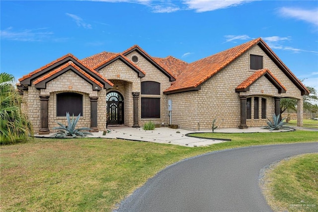 french country style house featuring a tile roof and a front lawn