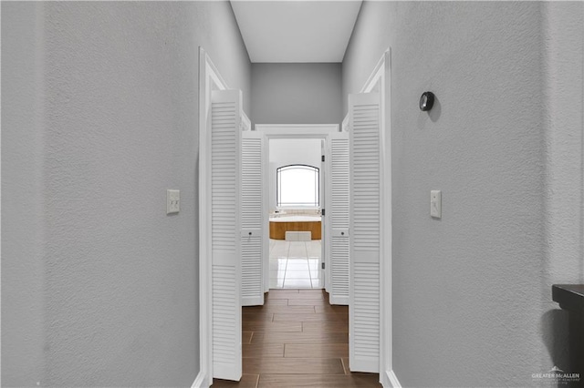 hallway with a textured wall, wood finish floors, and baseboards