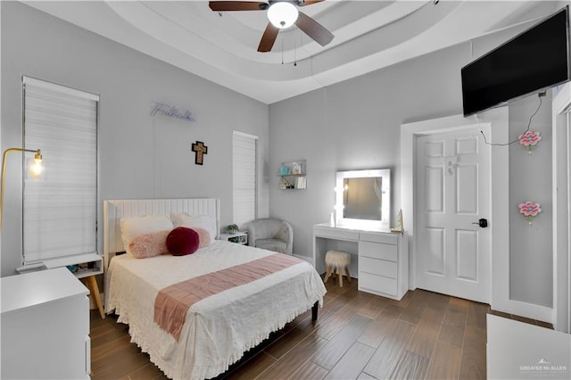 bedroom featuring dark wood-style flooring, a raised ceiling, a ceiling fan, and baseboards