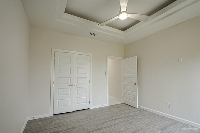 unfurnished bedroom featuring ceiling fan, a raised ceiling, light wood-type flooring, and a closet