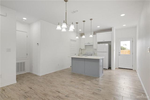 kitchen featuring white appliances, a kitchen island with sink, decorative light fixtures, white cabinets, and light hardwood / wood-style floors