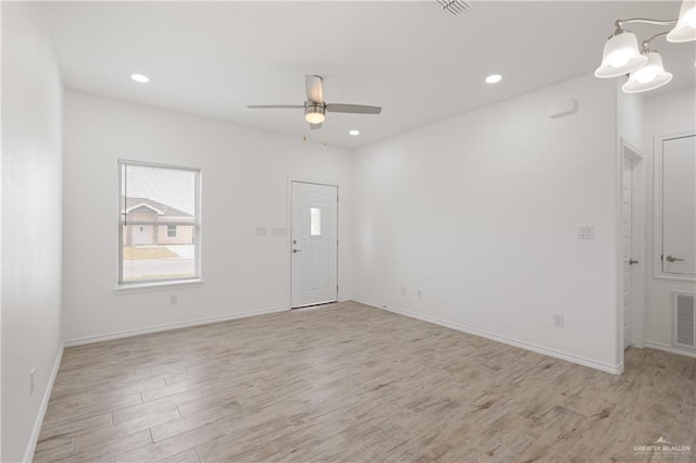 unfurnished room with ceiling fan with notable chandelier and light hardwood / wood-style floors