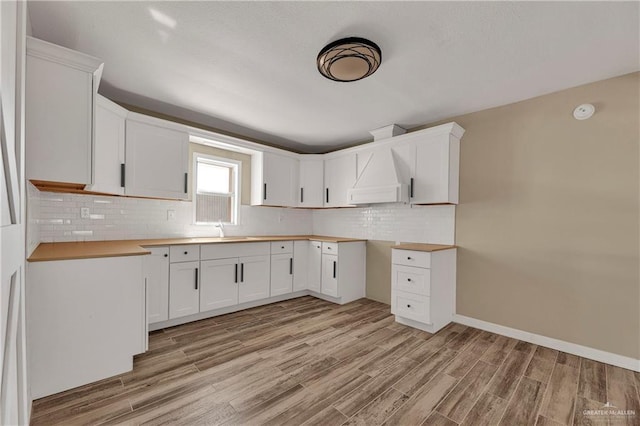318 E 2nd Ave, Elsa, TX 78543 - kitchen with light wood-style floors, a sink, backsplash, white cabinetry, and custom range hood