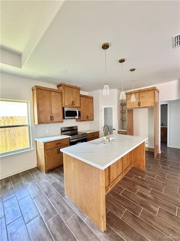 kitchen featuring sink, dark wood-type flooring, hanging light fixtures, a center island with sink, and appliances with stainless steel finishes