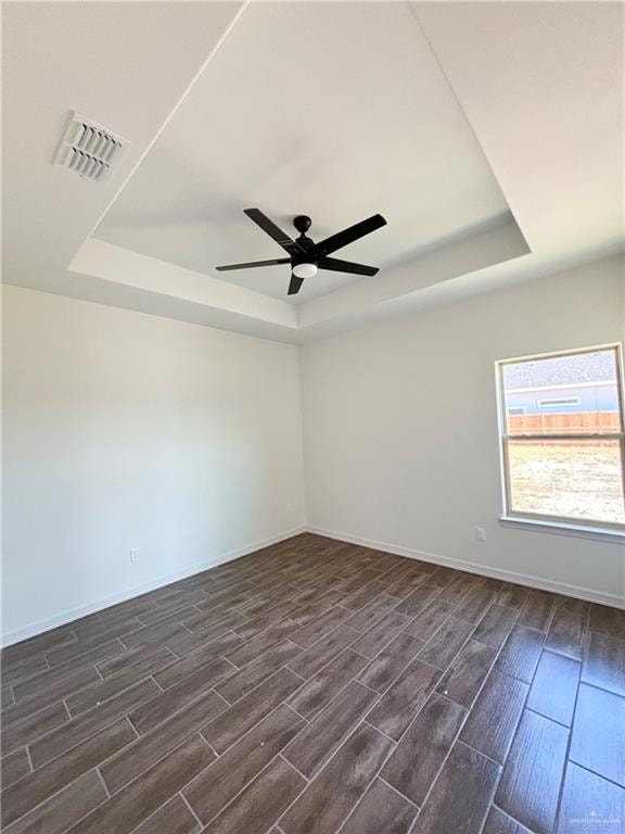 empty room with a raised ceiling, ceiling fan, and dark hardwood / wood-style flooring